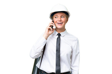 Young architect caucasian woman with helmet and holding blueprints over isolated background keeping a conversation with the mobile phone