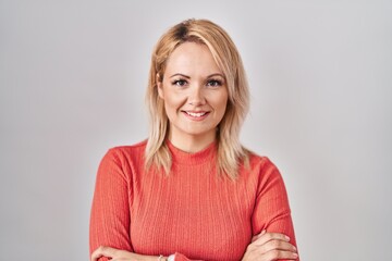 Obraz premium Blonde woman standing over isolated background happy face smiling with crossed arms looking at the camera. positive person.