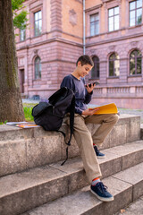 Obraz premium Joyous teen seated on the stairs outdoors using his cellphone