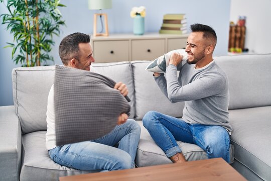 Two Men Couple Fighting With Cushion Sitting On Sofa At Home