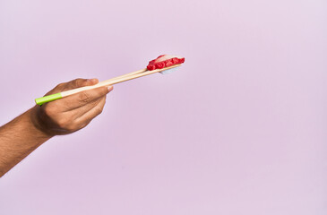  Hand of man holding octopus nigiri with chopsticks over isolated pink background