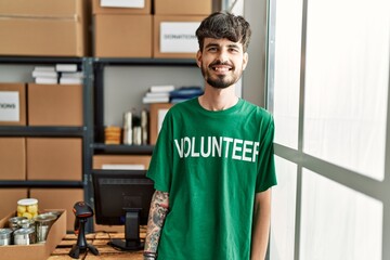 Young hispanic man wearing volunteer uniform standing at charity center.