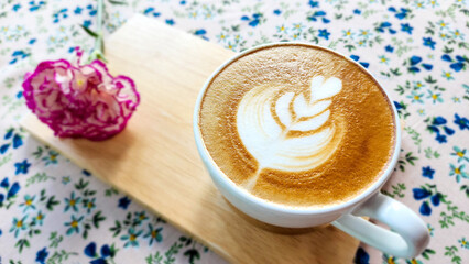 Latte art coffee tulip design in white cup on wodden plate on the  flower painting cloth background and there is a carnation flower beside