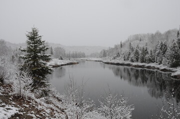 Winter Scenery Season Photo and Image.  Horizontal Photo.  Displaying its white blanket on trees, river and with a grey sky with a tranquillity feeling of peace.