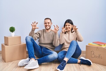 Young couple moving to a new home smiling funny doing claw gesture as cat, aggressive and sexy...