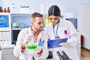 Fototapeta premium Man and woman wearing scientists uniform measuring liquid at laboratory