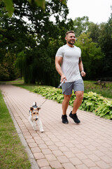 Naklejka na ściany i meble Portrait of joyful athlete running with his pedigreed dog in summer at nature.