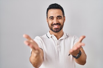 Fototapeta premium Young hispanic man with beard wearing casual clothes over white background smiling cheerful offering hands giving assistance and acceptance.