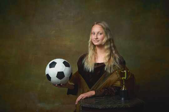 Football fan. Vintage style portrait of young charming girl in image of Mona Lisa, La Gioconda holding football ball isolated on dark background. Sport, betting, art