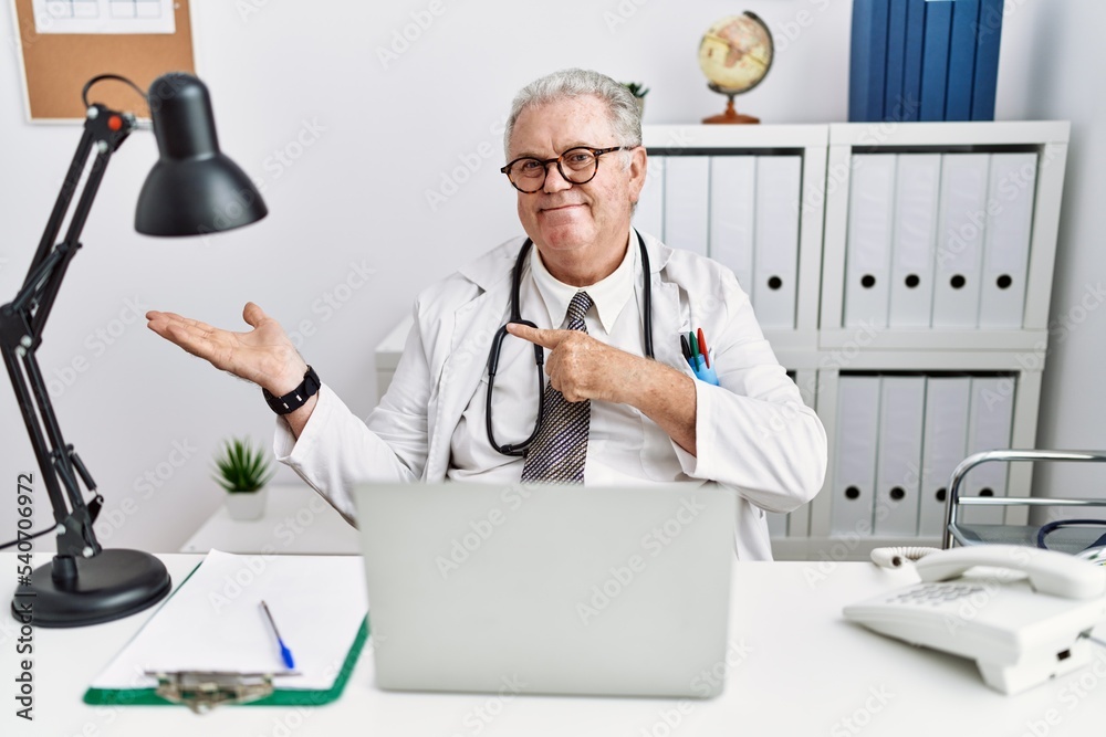 Sticker Senior caucasian man wearing doctor uniform and stethoscope at the clinic amazed and smiling to the camera while presenting with hand and pointing with finger.