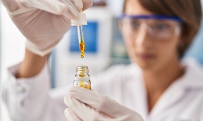Young beautiful hispanic woman scientist pouring liquid on test tube at laboratory