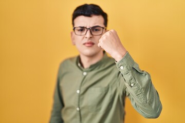 Obraz premium Non binary person standing over yellow background angry and mad raising fist frustrated and furious while shouting with anger. rage and aggressive concept.
