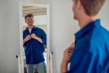 A confident young man getting dressed at the mirror