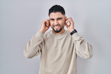 Fototapeta premium Young handsome man standing over isolated background covering ears with fingers with annoyed expression for the noise of loud music. deaf concept.