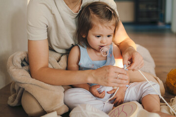 The baby child learning to embroider with a cross using a safe plastic needle and a cardboard trainer sitting on the floor in the living room. Home decoration.