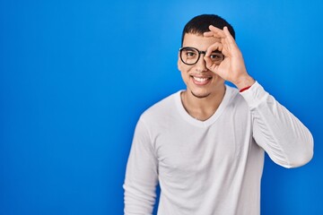 Naklejka premium Young arab man wearing casual white shirt and glasses doing ok gesture with hand smiling, eye looking through fingers with happy face.