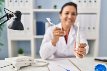 Middle age hispanic woman dentist holding toothbrushes at clinic