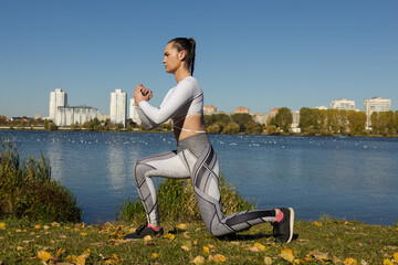 A young woman squats during a workout in the park. Training outside.