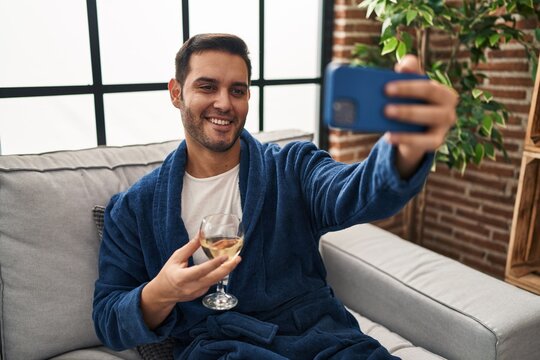 Young hispanic man make selfie by smartphone drinking wine at home