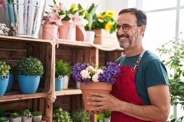 Middle age man florist holding plant of shelving at florist