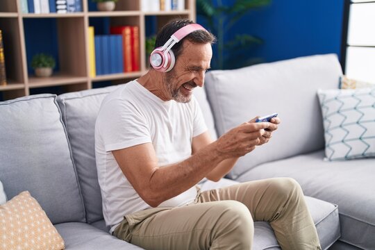 Middle age man playing video game sitting on sofa at home