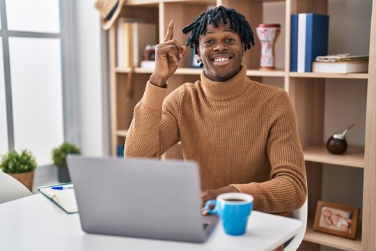 Young african man with dreadlocks working using computer laptop pointing finger up with successful idea. exited and happy. number one.
