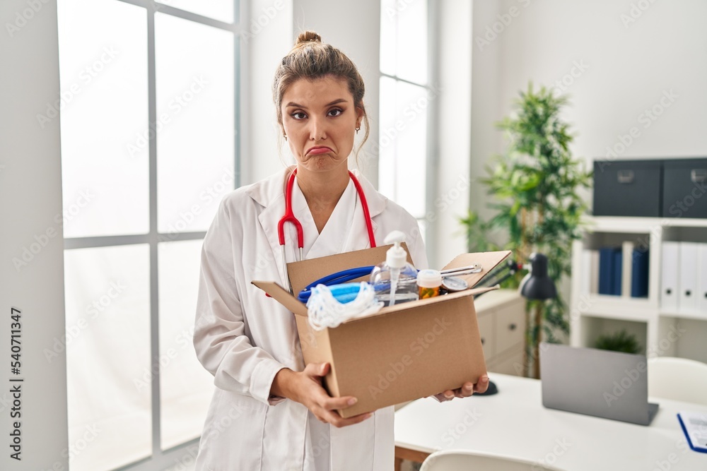 Poster young doctor woman holding box with medical items depressed and worry for distress, crying angry and