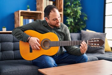 Young hispanic man playing classical guitar sitting on bed at home