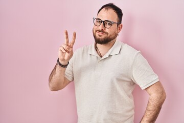 Plus size hispanic man with beard standing over pink background smiling looking to the camera...