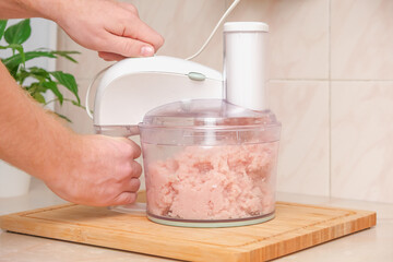 Food processor with pieces chicken breast. Process of cooking chicken fillet dishes. Mince, grind, knead, pure, shred a food processor of fresh raw chicken breast for cooking chopped chicken cutlets.