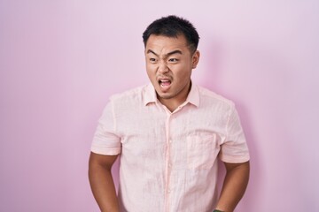 Chinese young man standing over pink background angry and mad screaming frustrated and furious, shouting with anger. rage and aggressive concept.