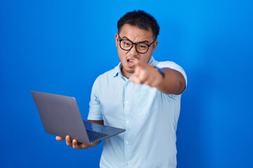 Chinese young man using computer laptop pointing displeased and frustrated to the camera, angry and furious with you