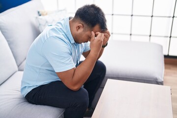 Fototapeta premium Young chinese man stressed sitting on sofa at home