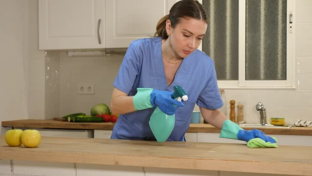  Woman professional cleaner cleaning desk with detergents in kitchen