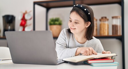 Young woman with down syndrome sitting on table studying at home