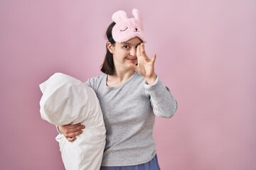 Woman with down syndrome wearing sleeping mask hugging pillow waiving saying hello happy and smiling, friendly welcome gesture