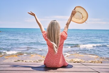 Young chinese girl on back view sitting on the bench with hands raised up at the beach.