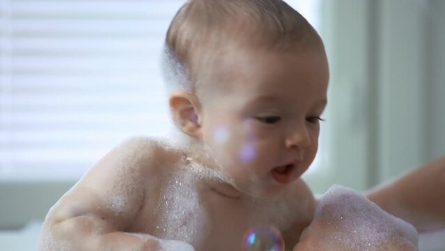 Cute healthy six month old baby bathing with foam and soap bubbles