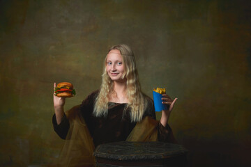Fast food. Happy young girl as Mona Lisa picture holding hamburger over dark vintage background. Retro style, art, fashion, comparison of eras concept.