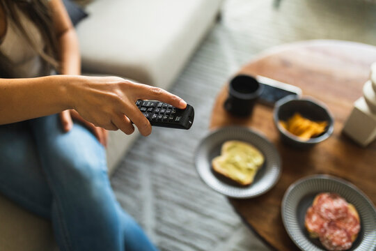 Young woman with TV remote control sitting at home