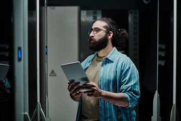 Technician holding tablet PC looking at server in data center
