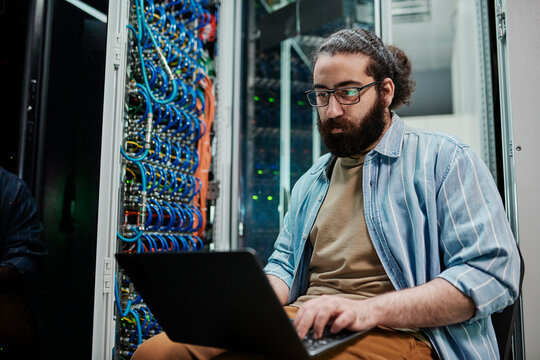 IT expert working on laptop sitting in server room