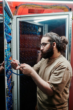 IT technician with beard connecting cables in server room