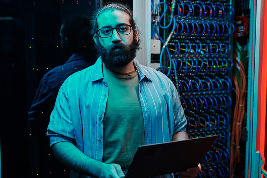 IT engineer with beard holding laptop in server room