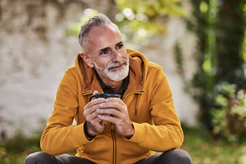 Smiling mature man sitting with coffee cup at park