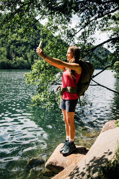 Hiker taking selfie through smart phone standing on rock near Lake Levico