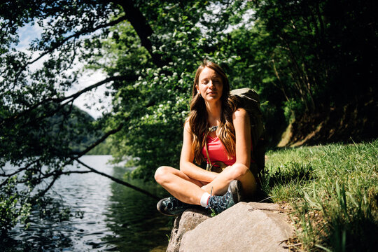Woman with eyes closed sitting cross-legged near Lake Levico