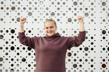 Smiling woman making fists in front of wall