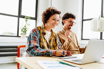 Happy graphic designer with colleague using laptop at desk in office