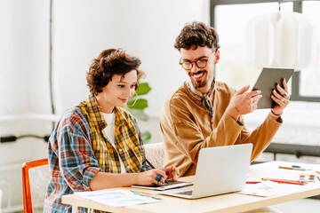 Happy illustrator with colleague using graphics tablet and laptop at desk